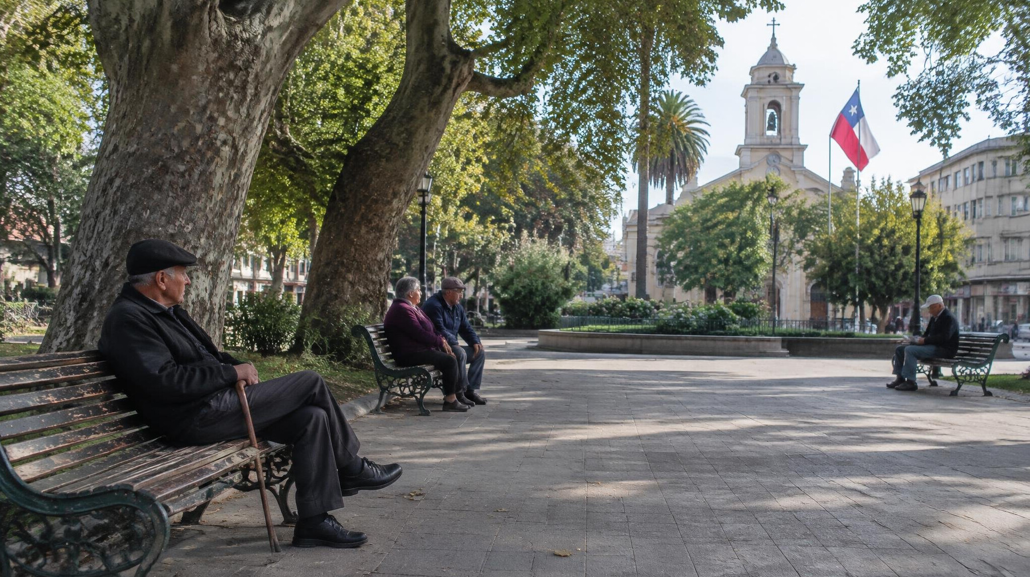 Elderly people sitting on benches in a quiet Chilean public plaza